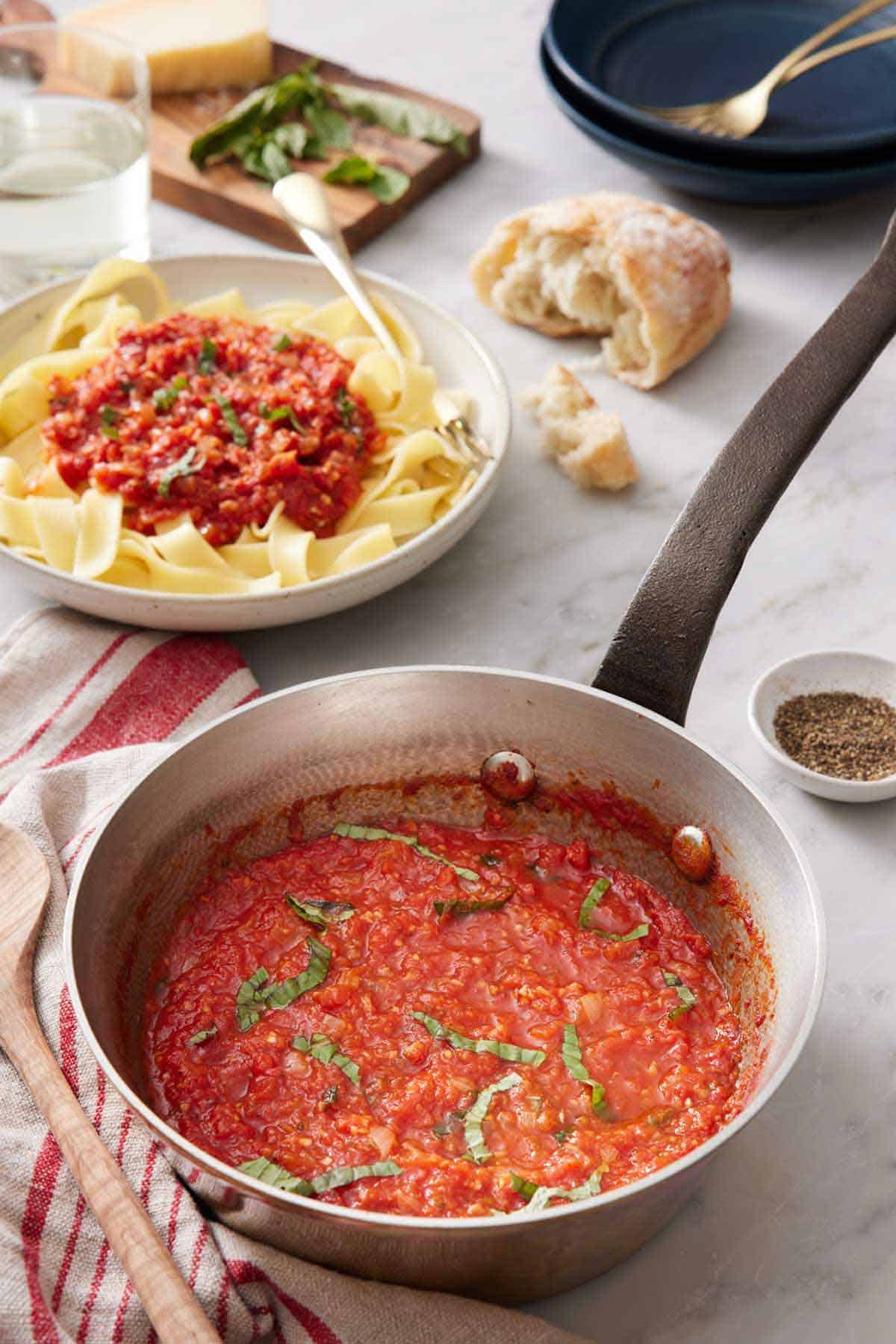 A pot of marinara sauce with torn bread in the back and a bowl of noodles with marinara sauce on top.