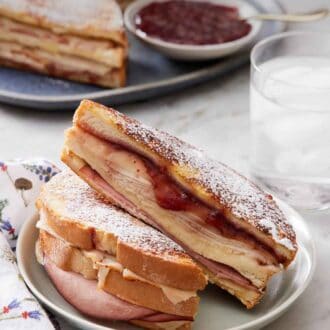 Pinterest graphic of a plate with a Monte Cristo sandwich cut in half with another one in the background along with a glass of water.