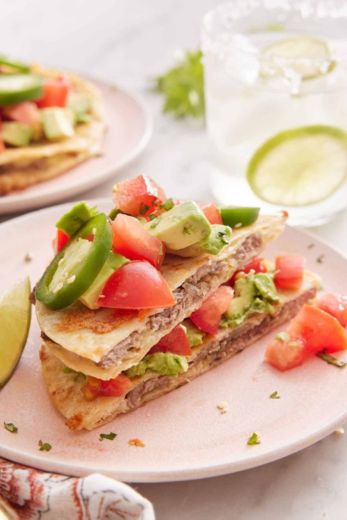 A plate with a mulita cut in half, stacked on top of each other, topped with jalapeno, tomatoes, and avocado.