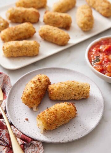 A plate with three air fryer mozzarella sticks with a platter in the background with more.