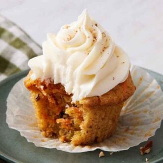 A small green plate with a carrot cake cupcake with a bite taken out of it.