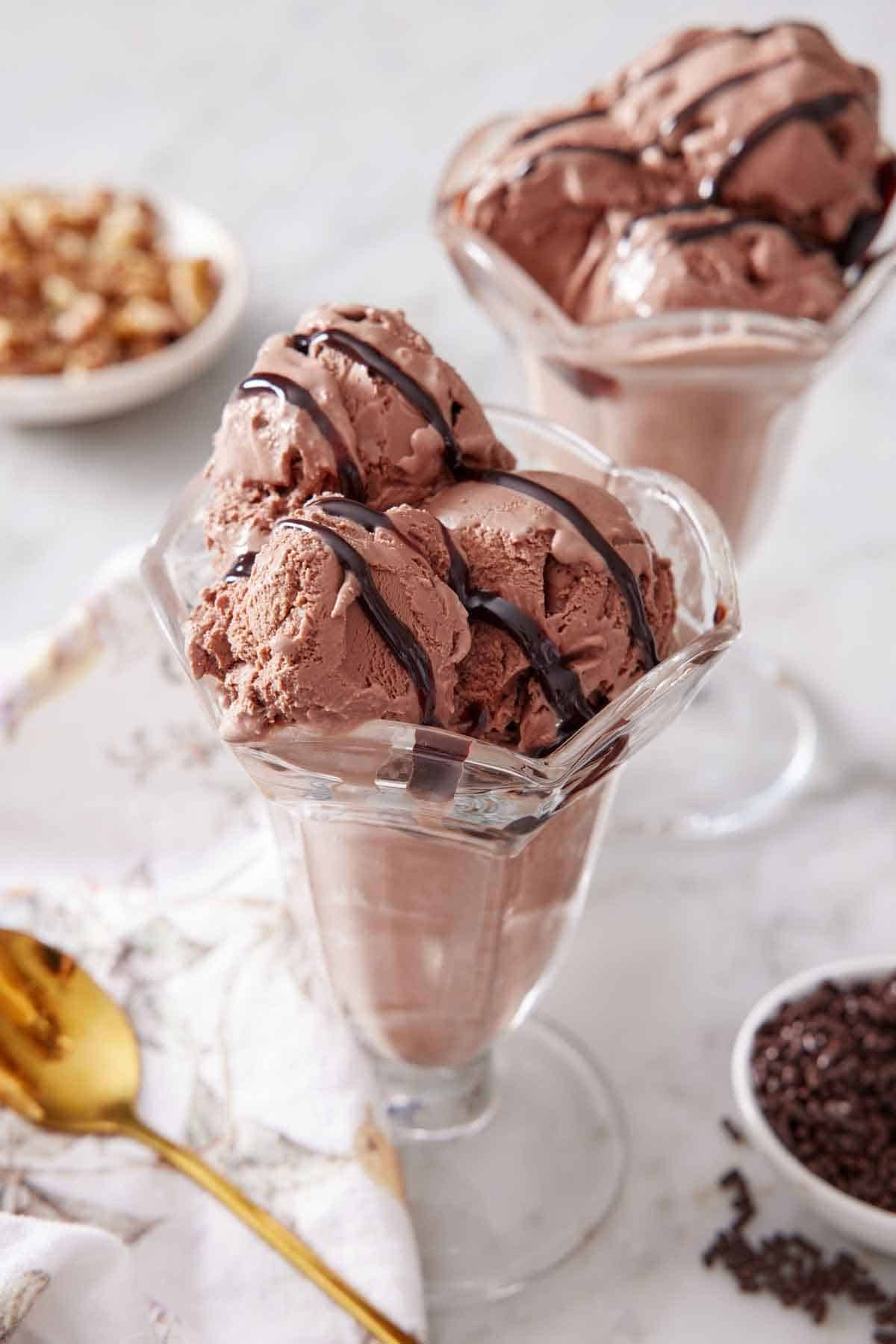 Two milkshake glasses with chocolate ice cream topped with chocolate drizzle.