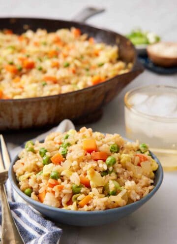 A bowl of fried rice with a skillet of more in the background along with a drink.