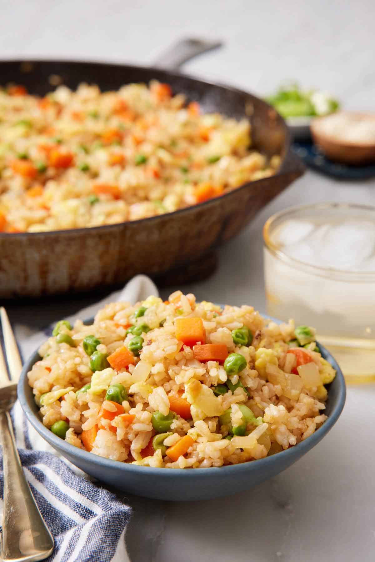 A bowl of fried rice with a skillet of more in the background along with a drink.