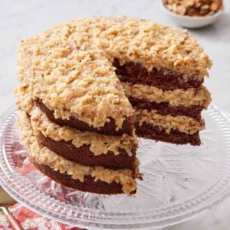 A cake stand with a German chocolate cake with a portion cut out.