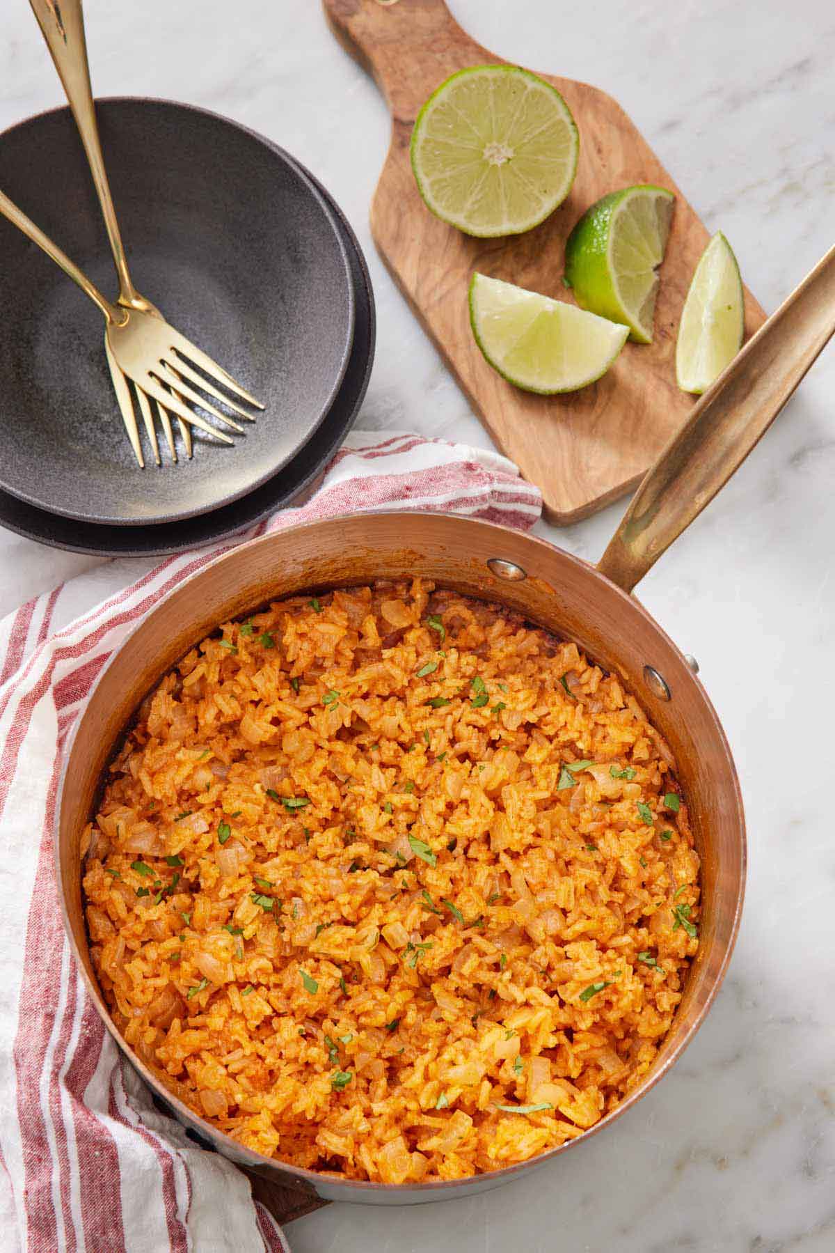 Overhead view of a pot of Mexican rice with bowls, forks, and cut limes off to the side.