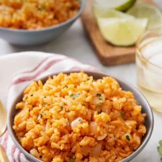 Pinterest graphic of a bowl of Mexican rice with a drink, cut limes, and a second bowl in the background out of focus.