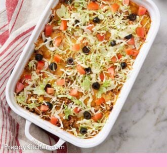 Pinterest graphic of a baking dish with a taco casserole topped with shredded lettuce, diced tomatoes, and olives. More toppings and tortilla chips on the side.