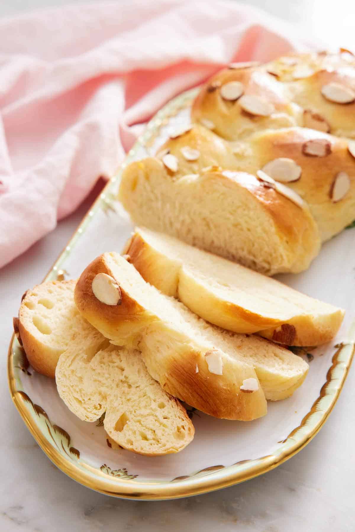 A platter with a loaf of tsoureki with three slices cut in front.