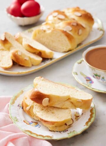 A plate with two slices of tsoureki with a coffee in the back along with a platter with the rest of the bread.