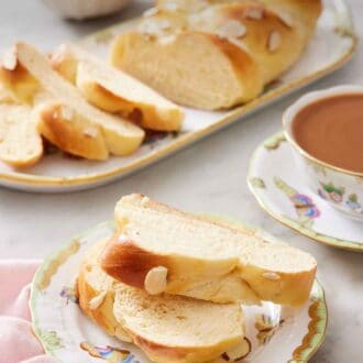 Pinterest graphic of a plate with two slices of tsoureki with a coffee in the back along with a platter with the rest of the bread.
