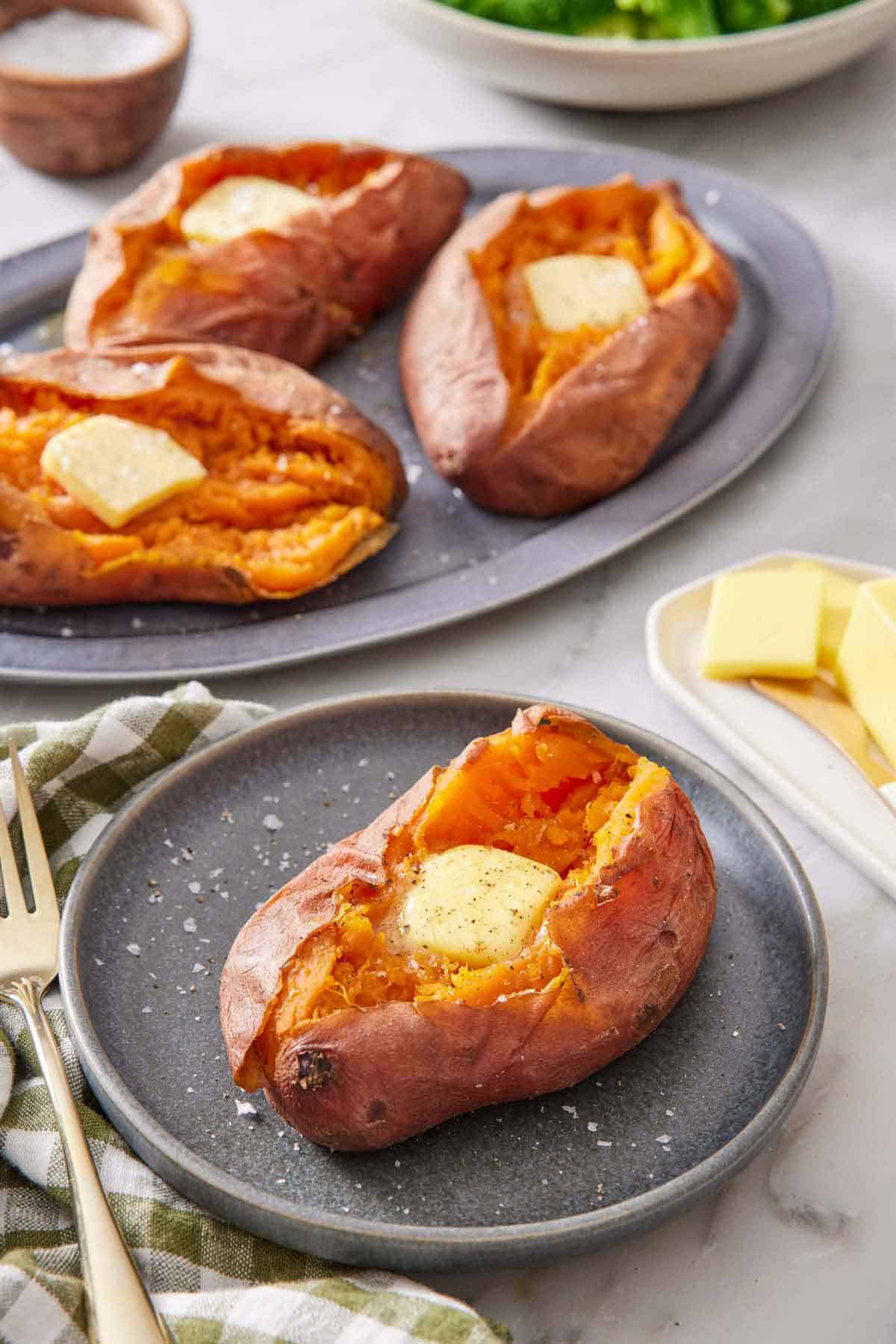 A plate with an instant pot sweet potato with a knob of butter in the middle. Three more with butter on a platter in the background.