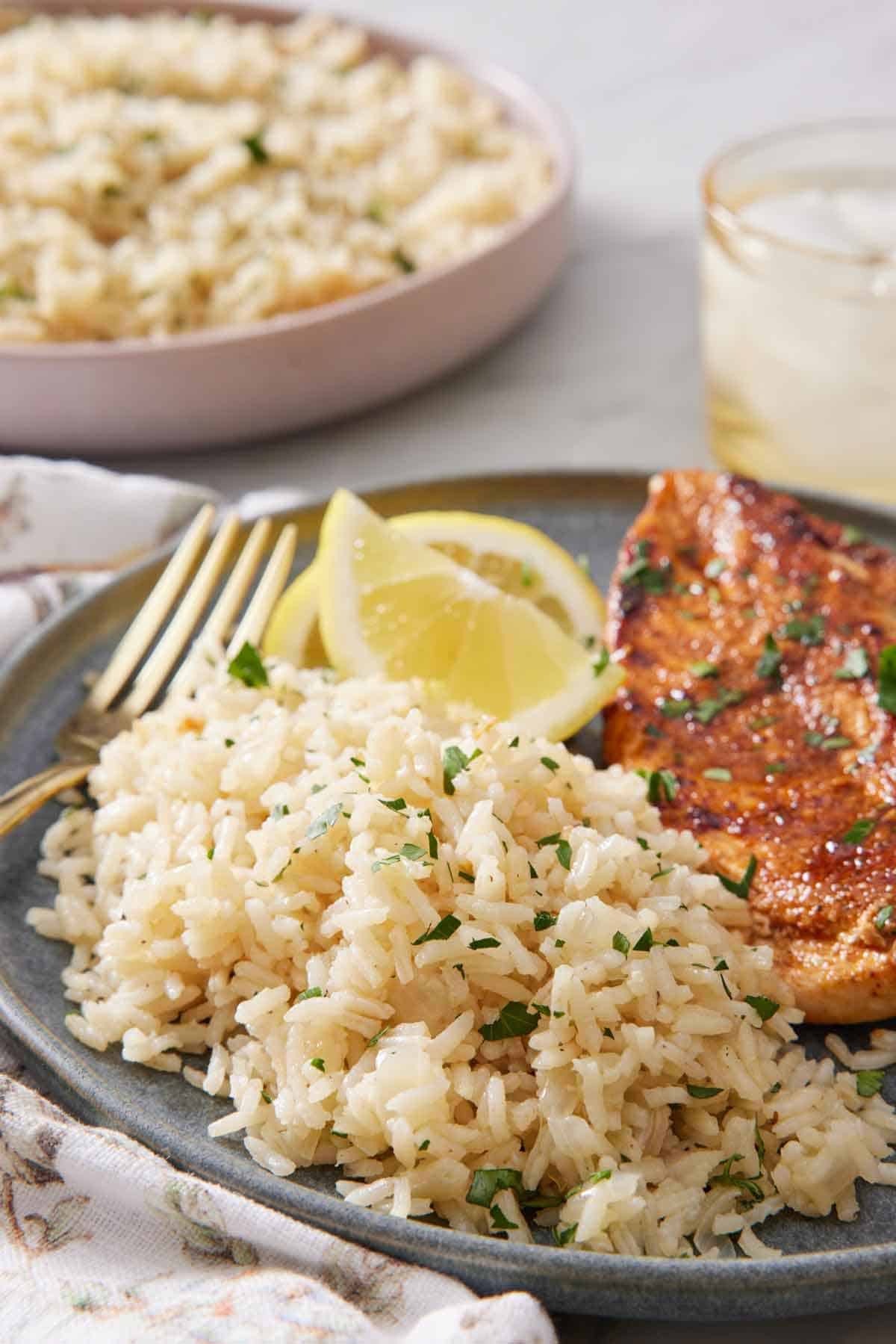 A plate with rice pilaf with lemon wedges and meat. A drink and another plate of rice in the background.