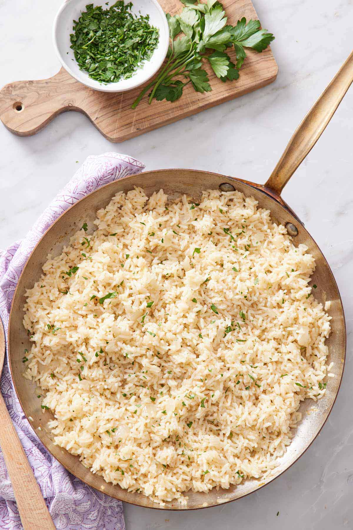 Overhead view of a skillet of rice pilaf with chopped parsley garnish. A wooden cutting board with chopped and whole parsley off to the side.