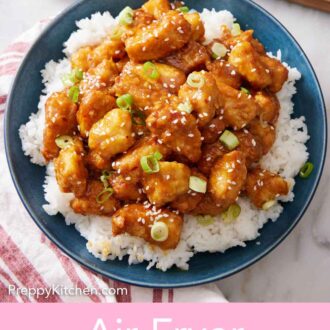 Pinterest graphic of a plate of rice with air fryer orange chicken on top. A bowl of green onions and some cut orange wedges in the back.