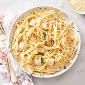 Overhead view of a plate of Instant Pot chicken alfredo with a fork and bowl of cheese beside it.