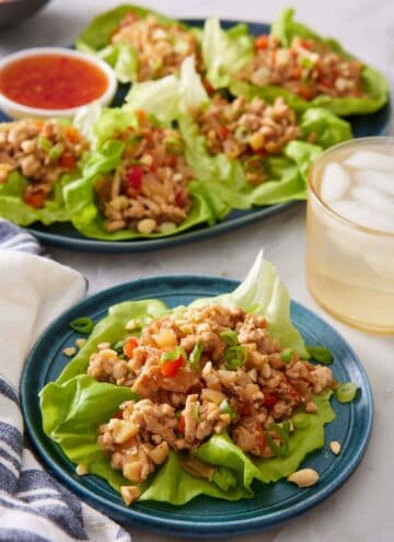 A plate with a lettuce wrap with more in the back on a platter with an iced drink.