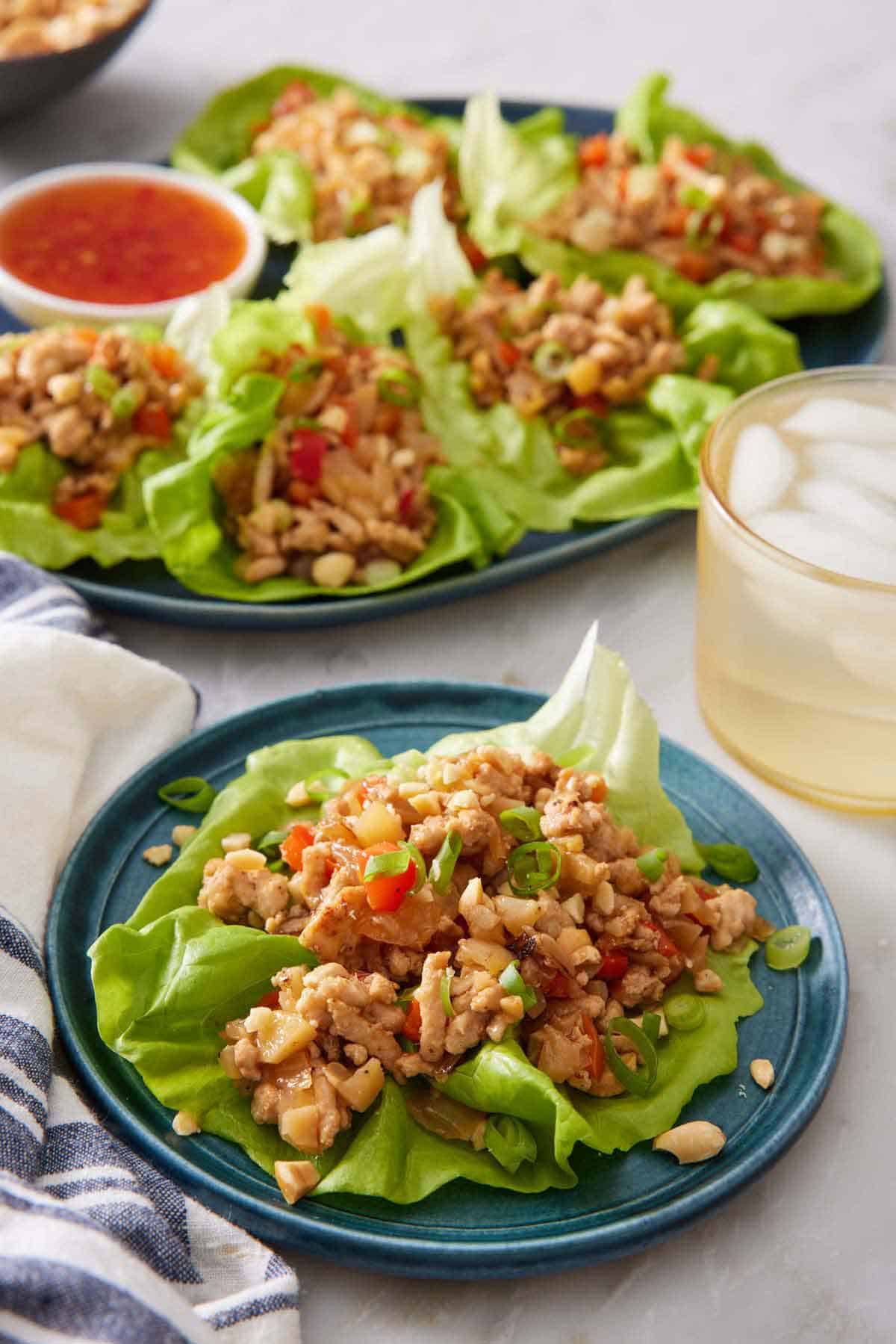 A plate with a lettuce wrap with more in the back on a platter with an iced drink.