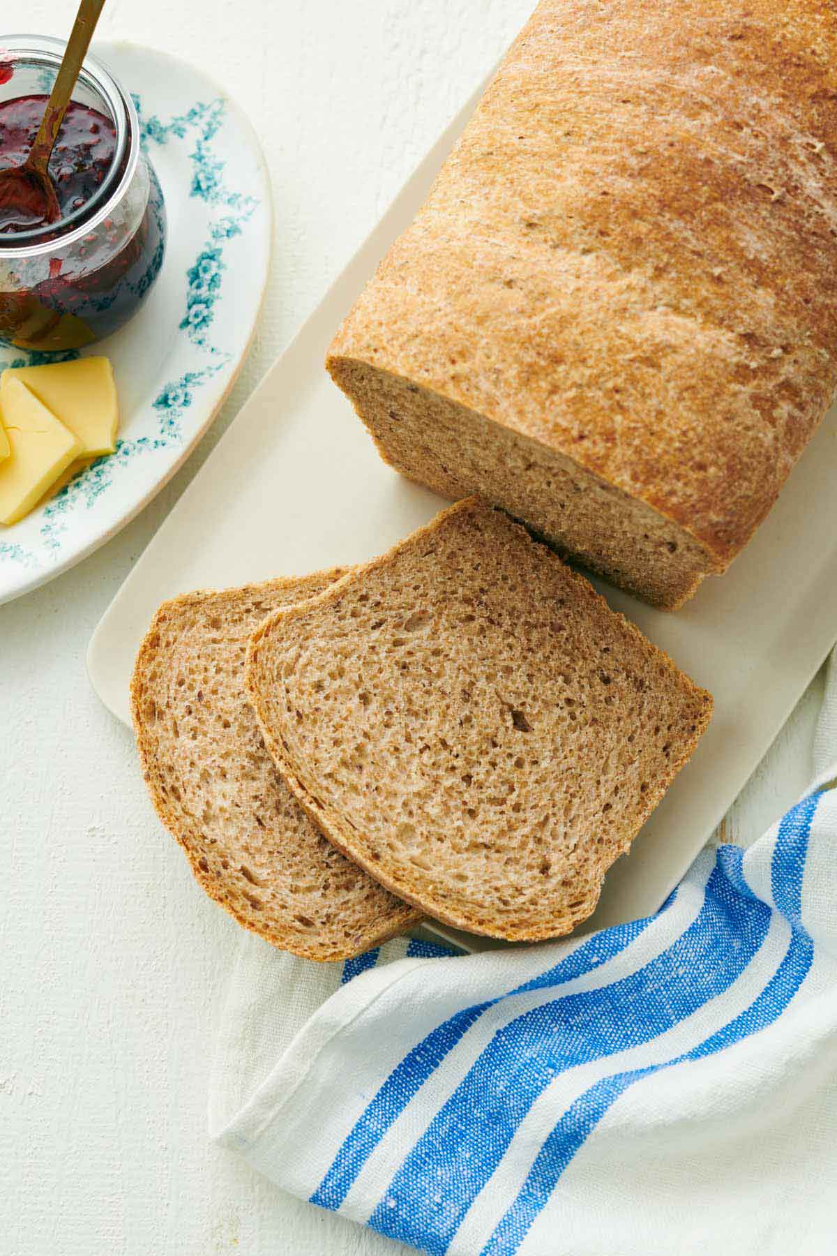 Overhead view of a loaf of rye bread with two slices cut. Jam and butter off to the side.