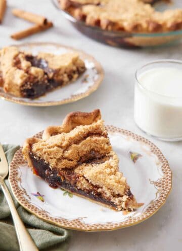 A plate with a slice of shoofly pie with a glass of milk, another plated serving, and the rest of the pie in the background.