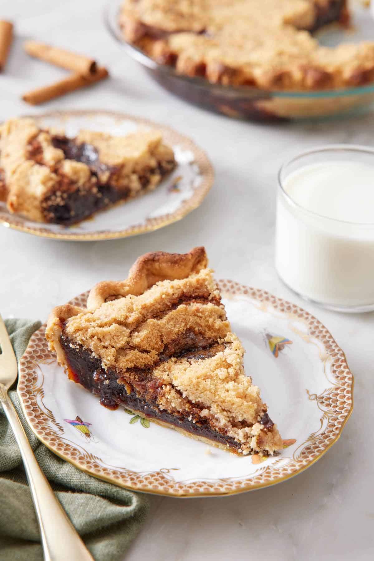 A plate with a slice of shoofly pie with a glass of milk, another plated serving, and the rest of the pie in the background.