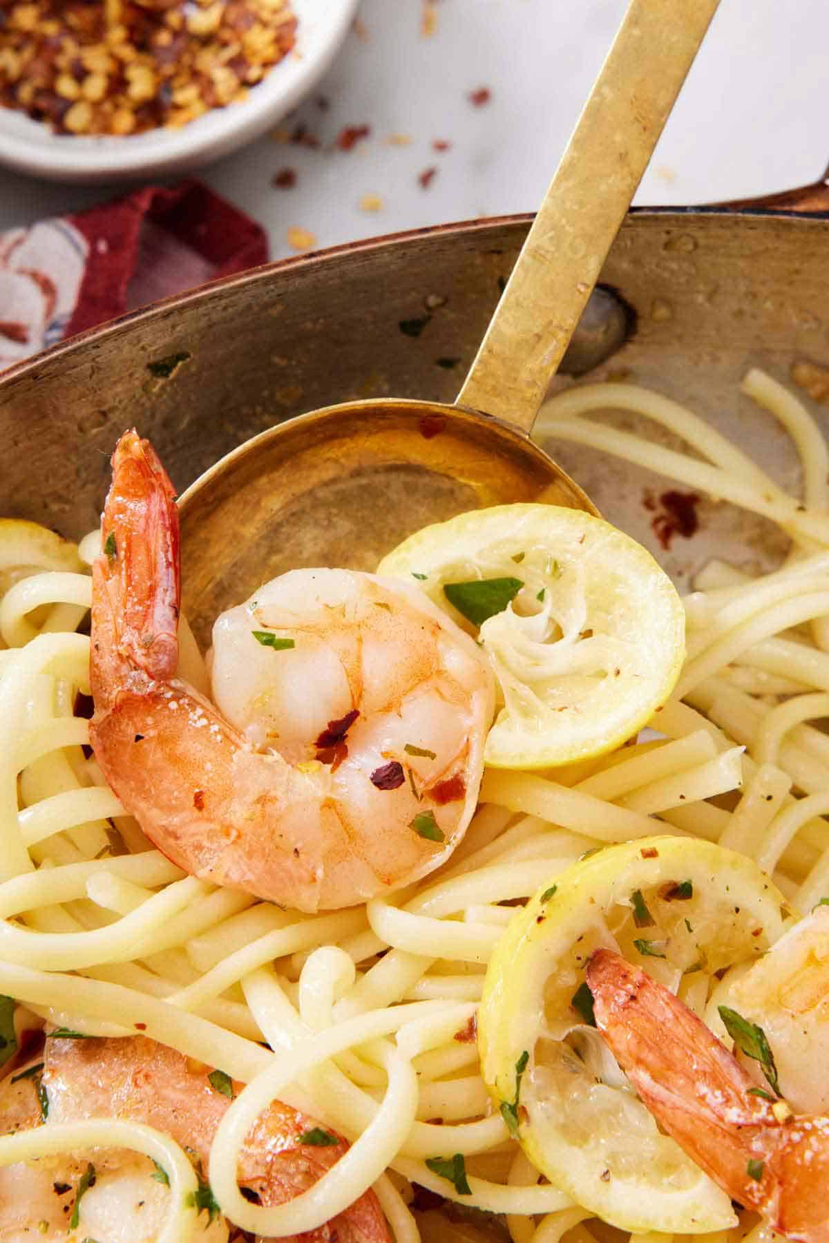 A close up view of a spoon serving up some shrimp linguine from a skillet.