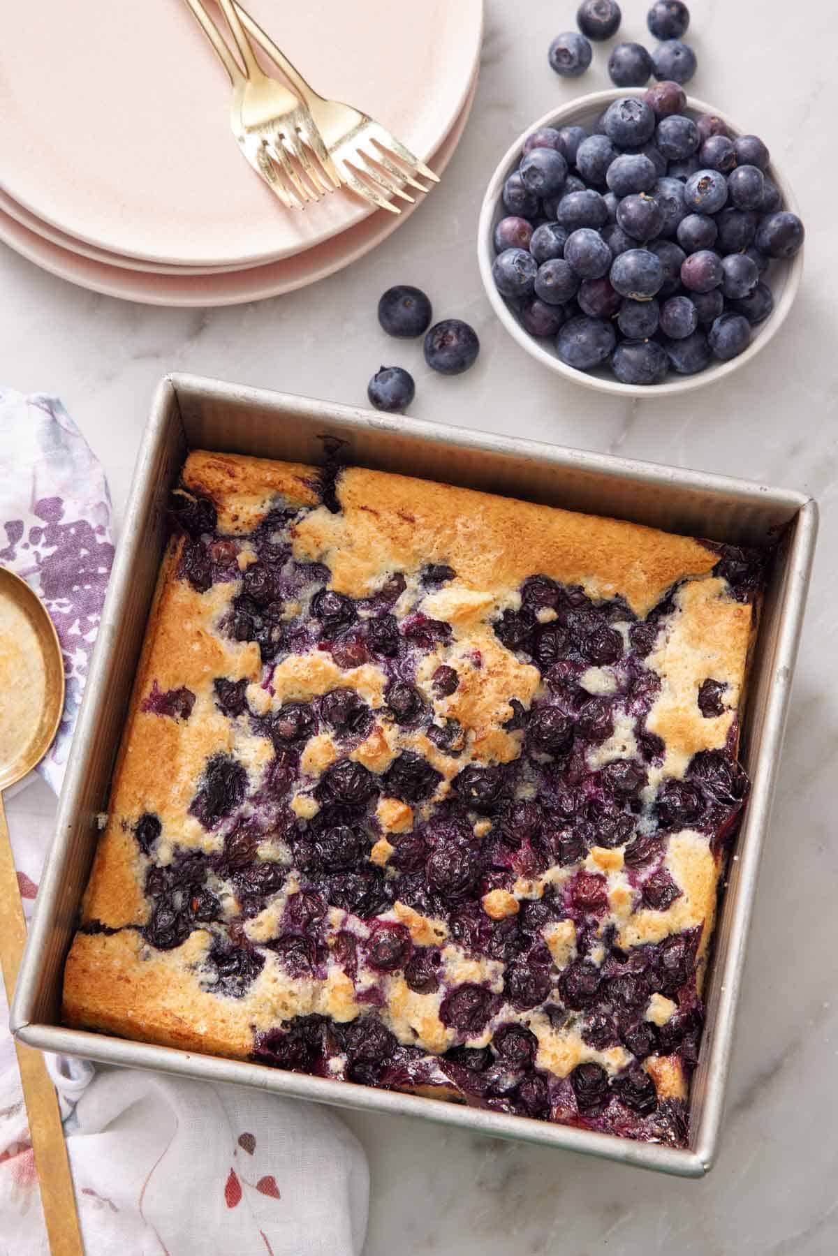 Overhead view of a blueberry cobbler in a pan with a bowl of blueberries on the side.