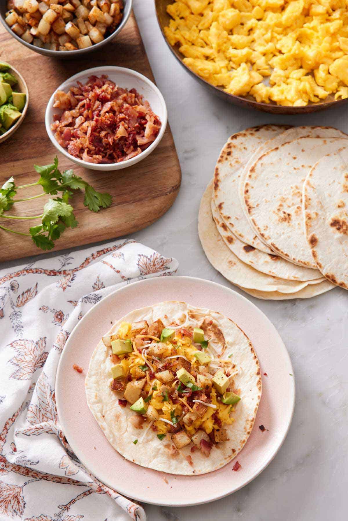 An overhead view of a plate with a breakfast taco with an assortment of toppings beside it.