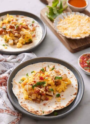 A plate with a breakfast taco with another plate in the background along with assorted toppings.