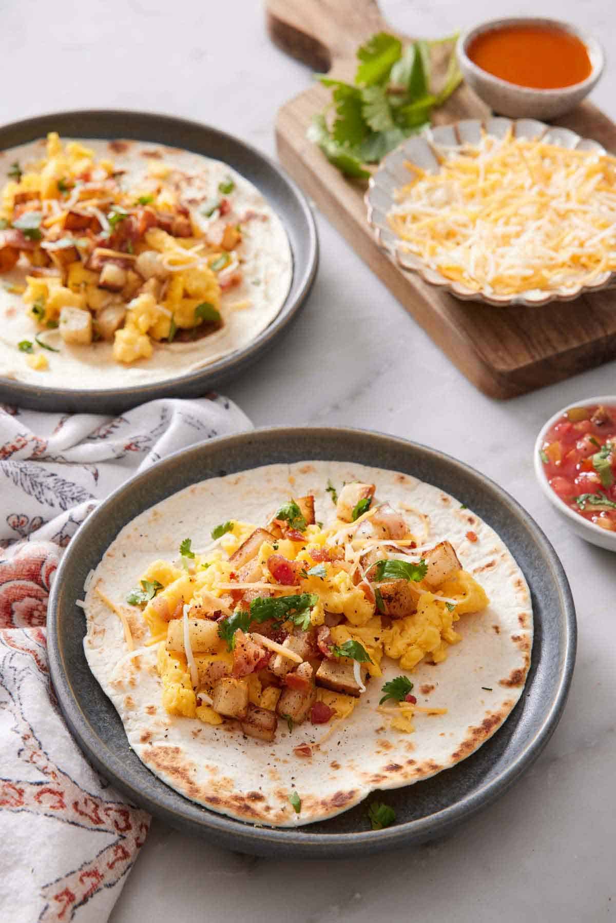 A plate with a breakfast taco with another plate in the background along with assorted toppings.