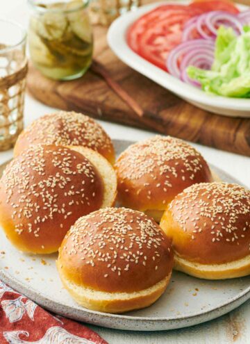 A platter with multiple burger buns. Toppings in the background.