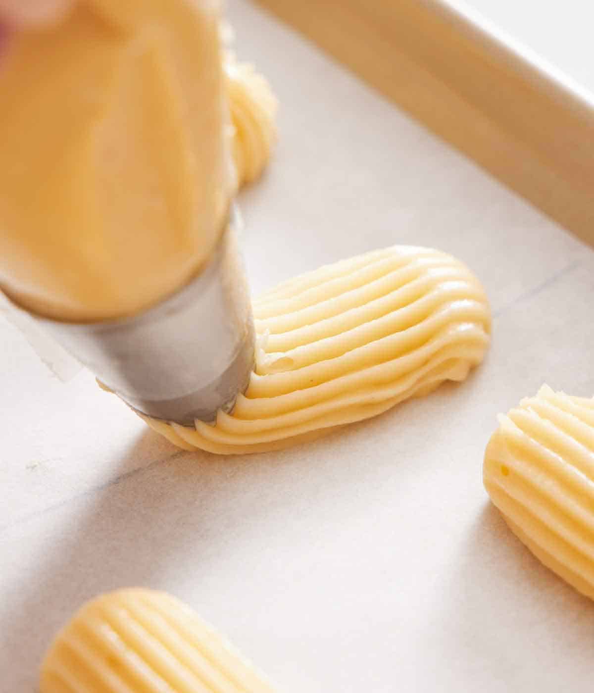 A lined sheet pan with eclairs batter piped onto it.