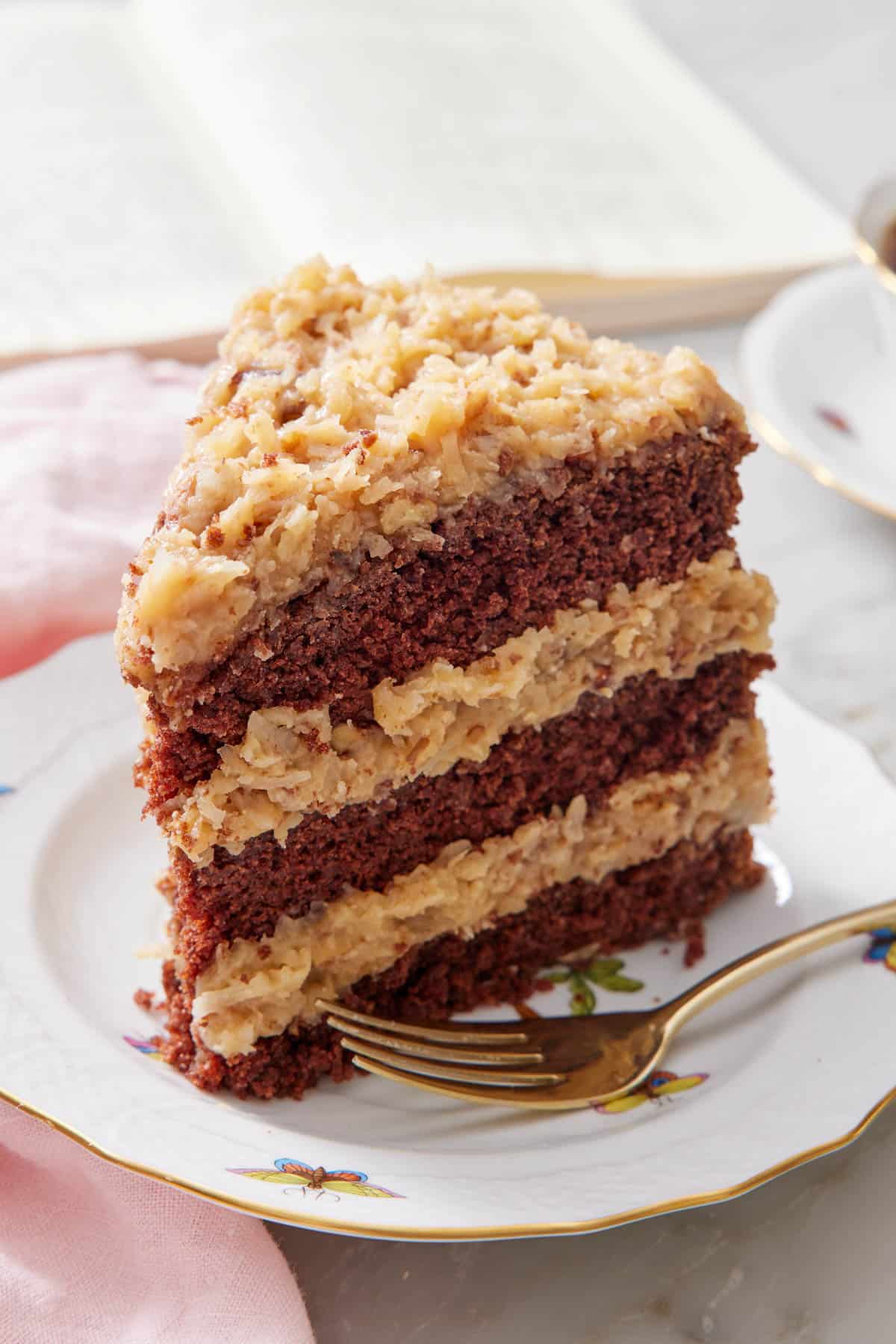 A slice of German chocolate cake on a plate with a fork beside it.