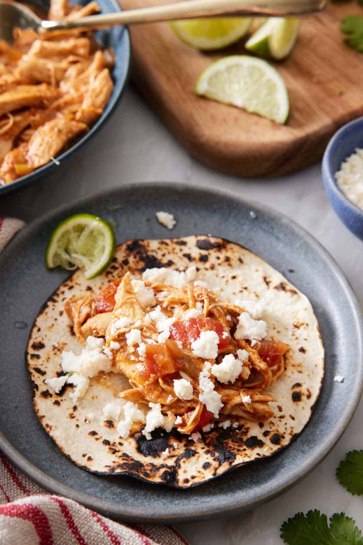A plate with an opened Instant Pot chicken tacos with crumbled cheese on top.