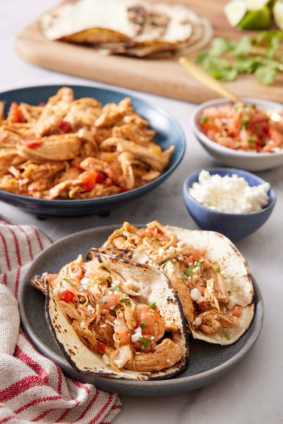 A plate with two Instant Pot chicken tacos with the rest of the components in the background.