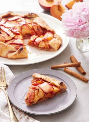 A plate of peach galette on a plate with the rest of the galette in the background.