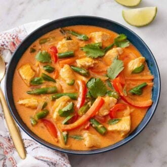 Overhead view of a bowl of Thai red curry with a spoon and lime wedges beside it.