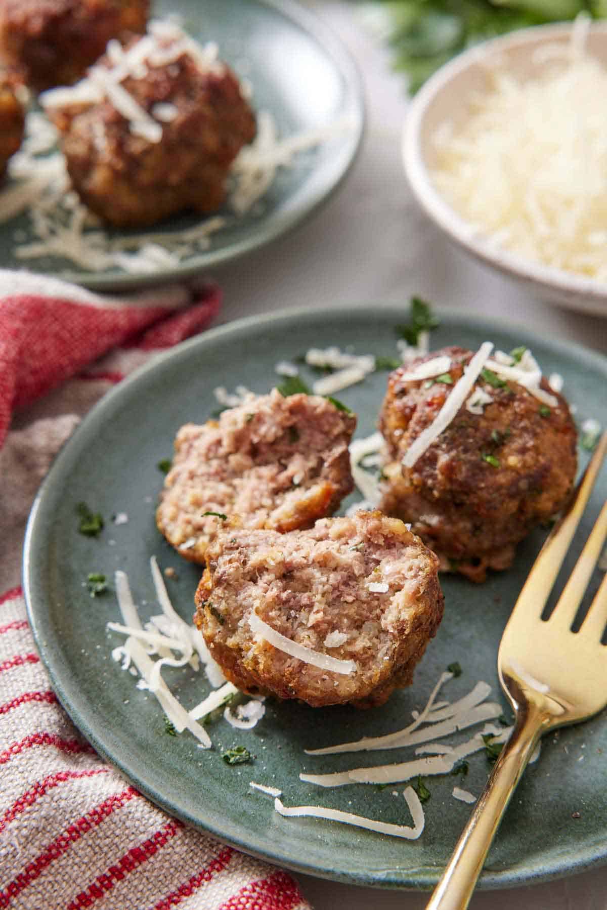 A plate with air fryer meatballs and a fork. One meatball cut opened. Shredded parmesan on top.