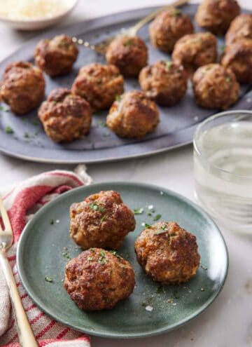 A plate with three air fryer meatballs with a platter more in the background with a drink in-between.