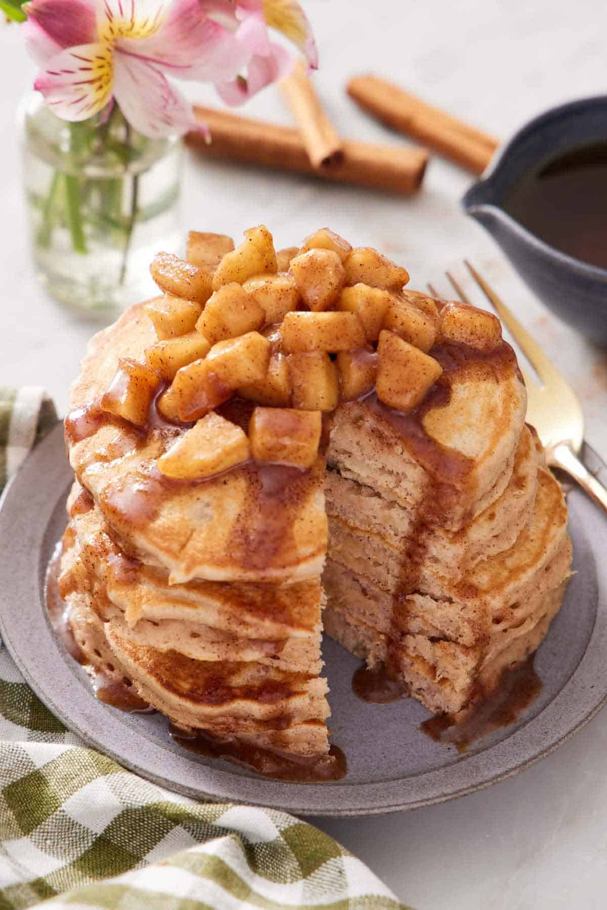 A stack of apple pancakes with apples and syrup on top with a slice cut out.