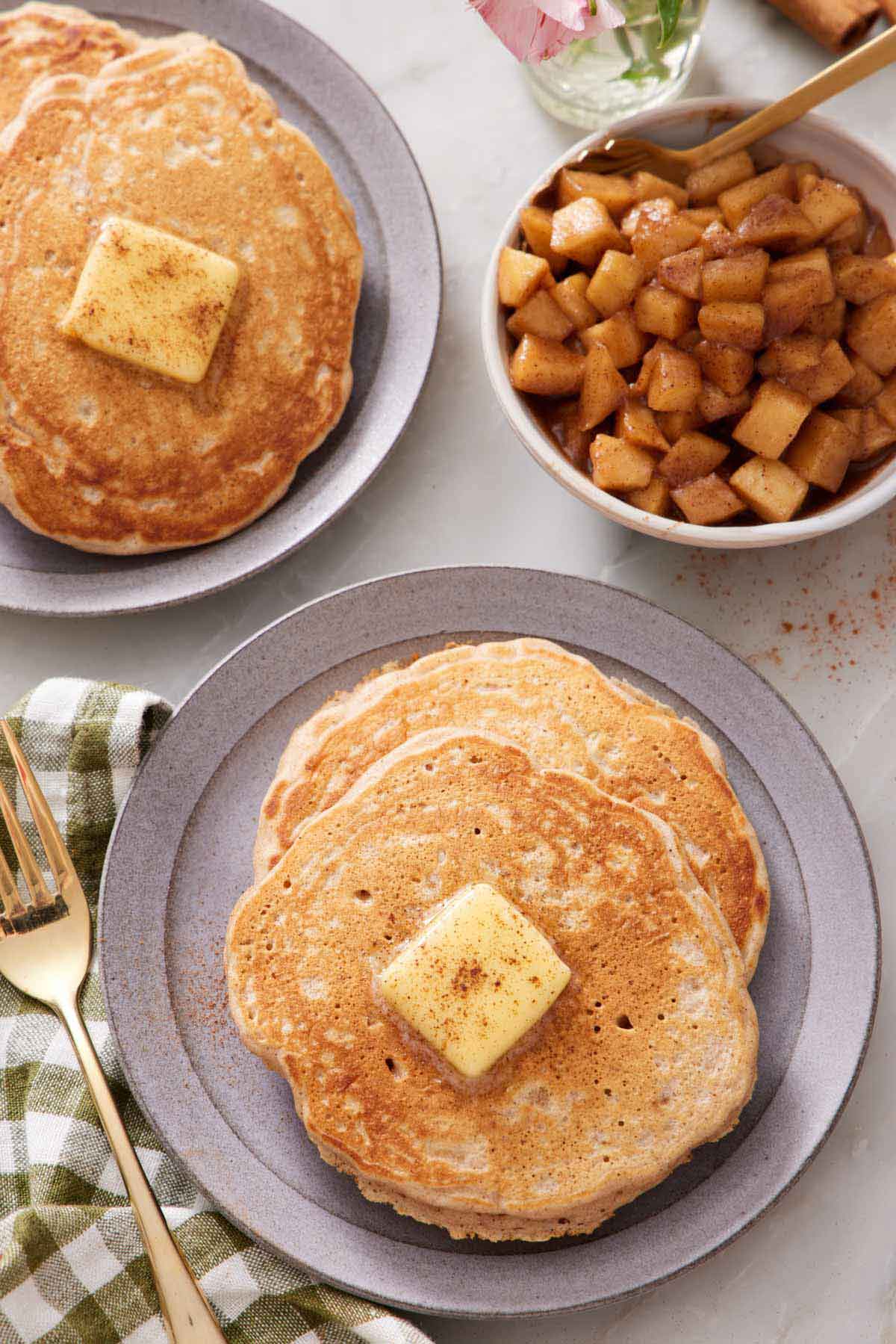 Overhead view of two plates with apple pancakes topped with butter and cinnamon.
