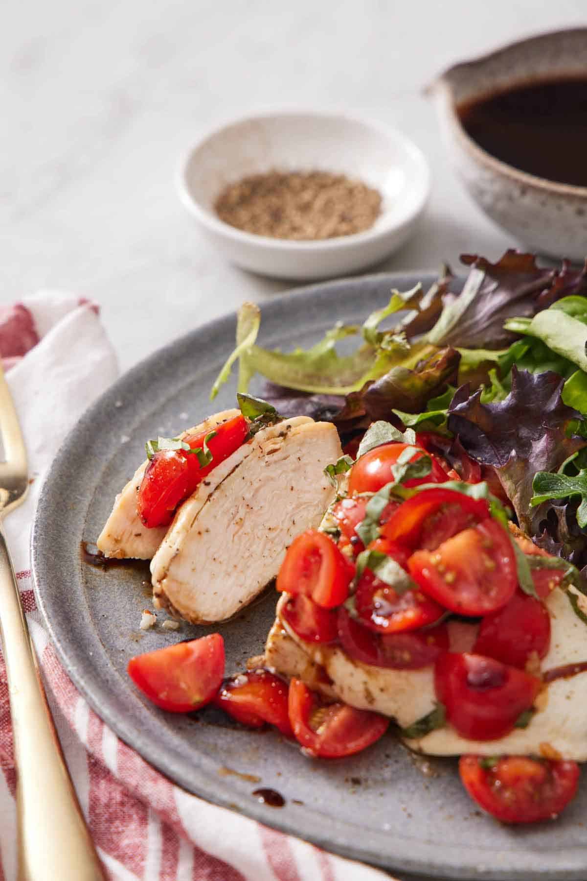 A plate with a bruschetta chicken breast with two bites cut. Some mixed greens beside it.