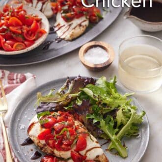 Pinterest graphic of a plate with bruschetta chicken and mixed greens. A platter of more bruschetta chicken, a drink, and bowl of tomatoes in the background.