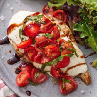 A close up view of bruschetta chicken topped with fresh basil and tomatoes with mixed greens beside it.