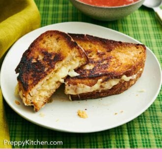 Pinterest graphic of a plate with a grilled cheese cut in half, one half leaning up against the other. Bowl of tomato soup in the background.