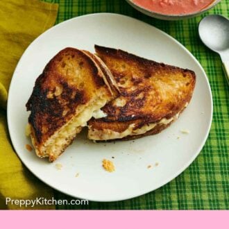 Pinterest graphic of an overhead view of a plate with a grilled cheese cut in half, one half leaning up against the other. A bowl of soup beside it.