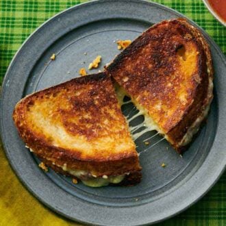 Overhead view of a plate with a grilled cheese cut in half, slightly pulled apart.