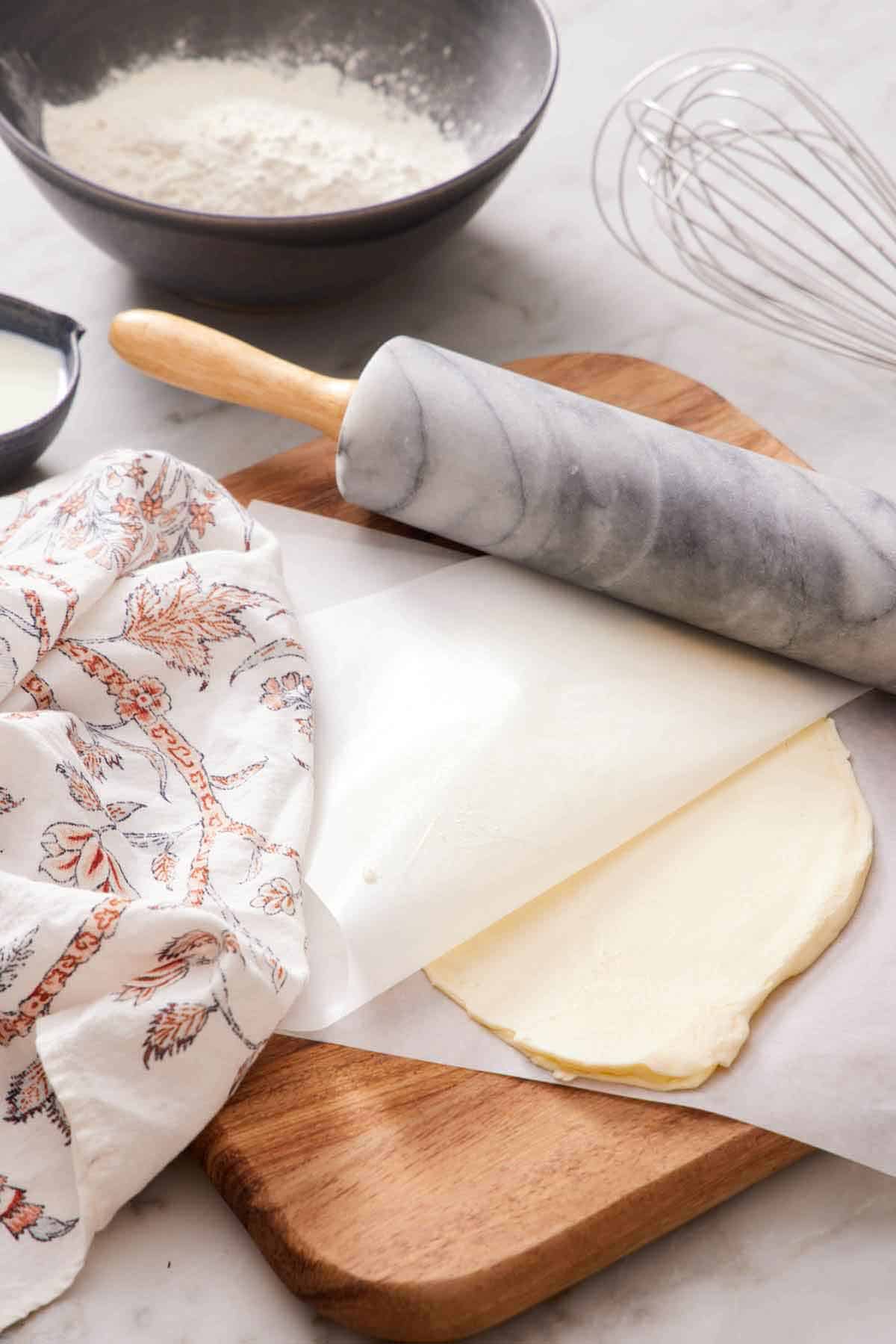 Softened butter rolled between two sheets of parchment with a rolling pin. A bowl of flour and a whisk in the background.