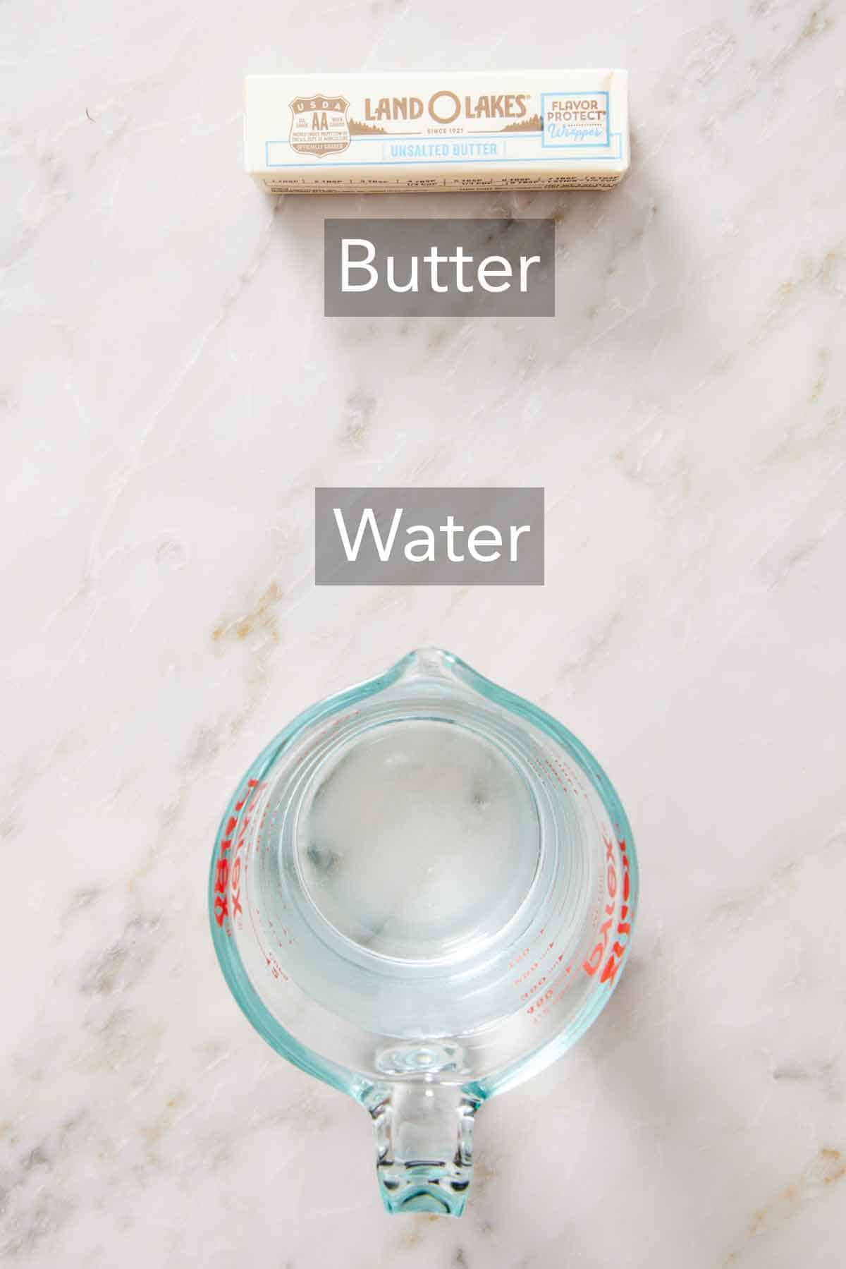Overhead view of a stick of butter and measuring cup of water.