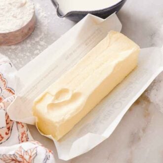 A stick of softened butter in an opened wrapper. A bowl of flour, sugar, and dairy surrounding it.